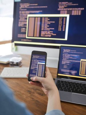 Vertical close up of female hand holding smartphone with code on screen while working at desk in office, female IT developer concept, copy space